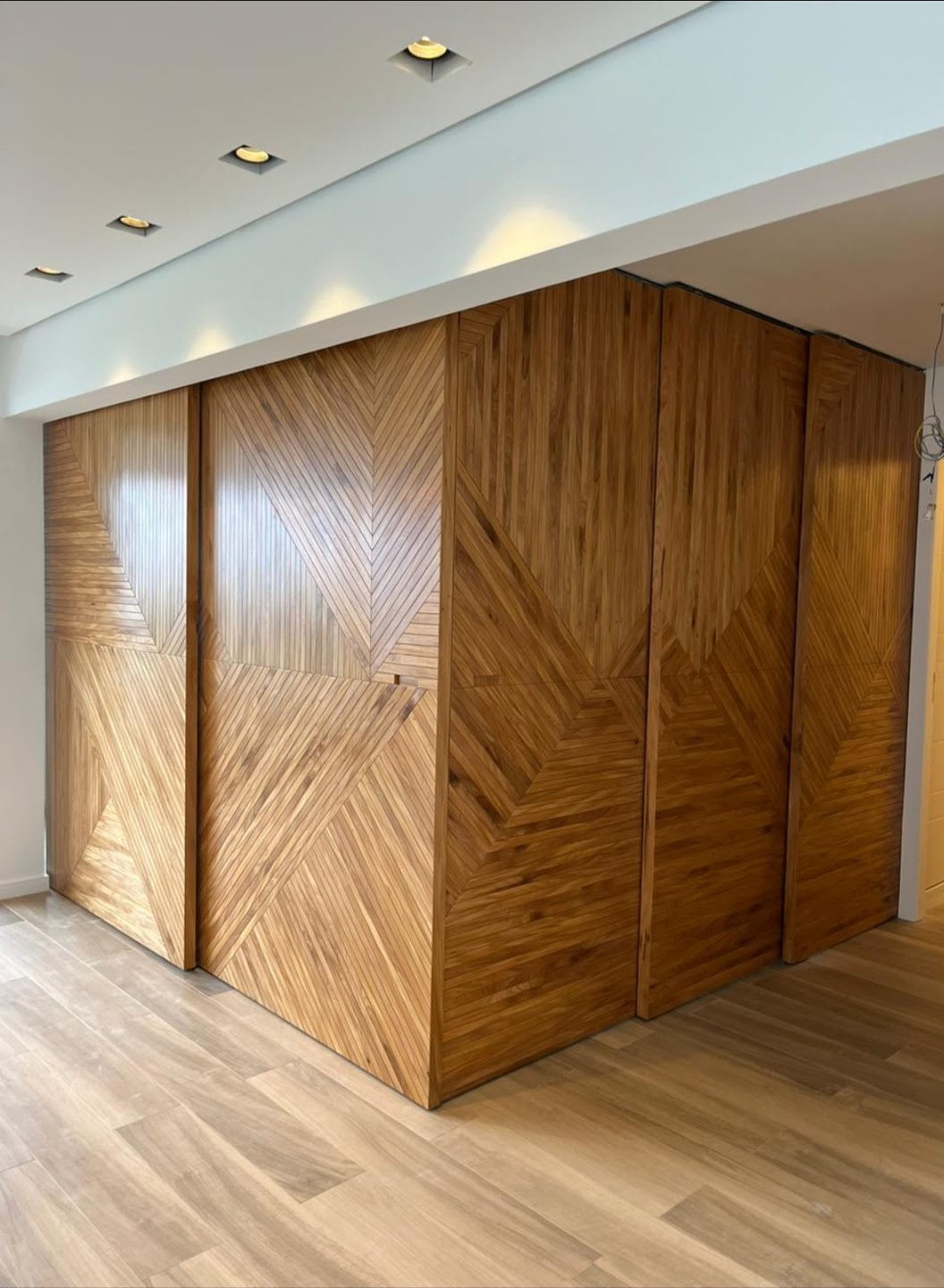 Conjunto de portas em ripas visto de canto, com iluminação embutida no teto