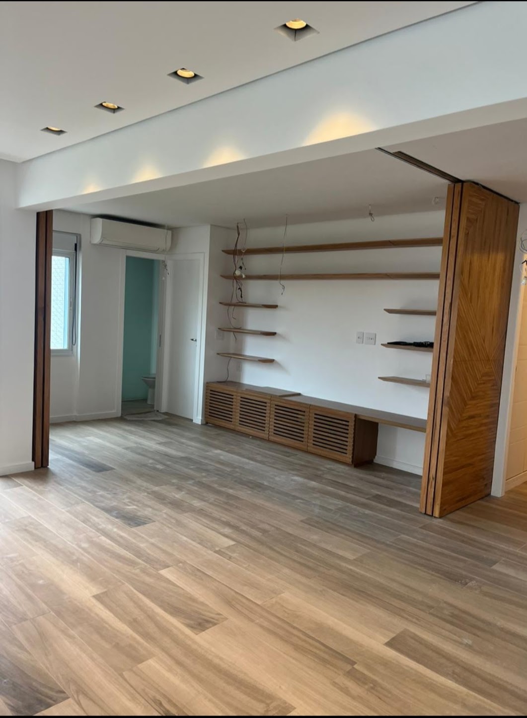 Sala com as portas em ripas abertas, estante de prateleiras e rack com frente vazada